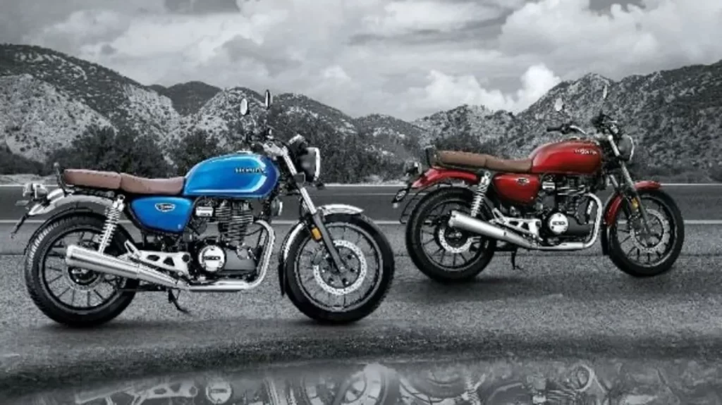 Honda GST Price Cut - A two-tone gray-scale and color photo showing two Honda H'ness CB350 motorcycles. The one in front is a striking blue, while the one behind is a vibrant red, with a blurred mountain background.