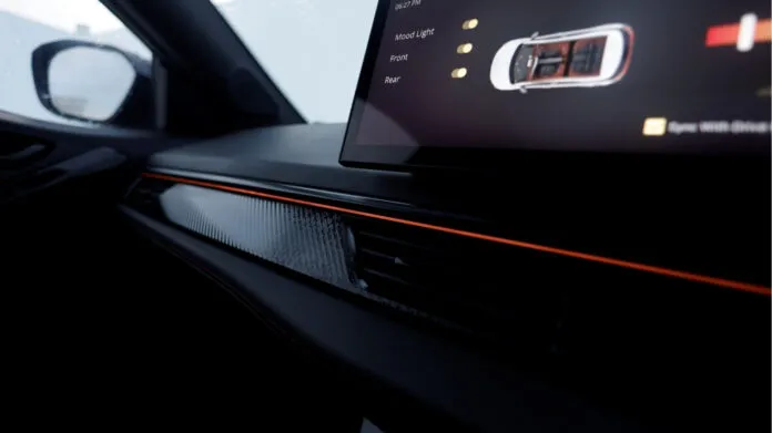 A close-up interior shot of the Tata Nexon EV's dashboard, highlighting the new ambient lighting feature. An orange light strip runs across the dashboard, and a digital screen displays the "Mood Light" controls.