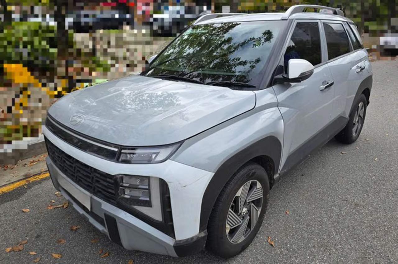 लीक हुई तस्वीर जिसमें हल्के ग्रे/सिल्वर रंग में New-Gen Hyundai Venue का फ्रंट क्वार्टर व्यू दिख रहा है, जिसमें बिल्कुल नया स्प्लिट हेडलैंप डिज़ाइन, क्षैतिज स्लैट्स वाली आयताकार ग्रिल, बोल्ड फ्रंट बम्पर और मोटी काली व्हील आर्च क्लैडिंग दिखाई गई है।