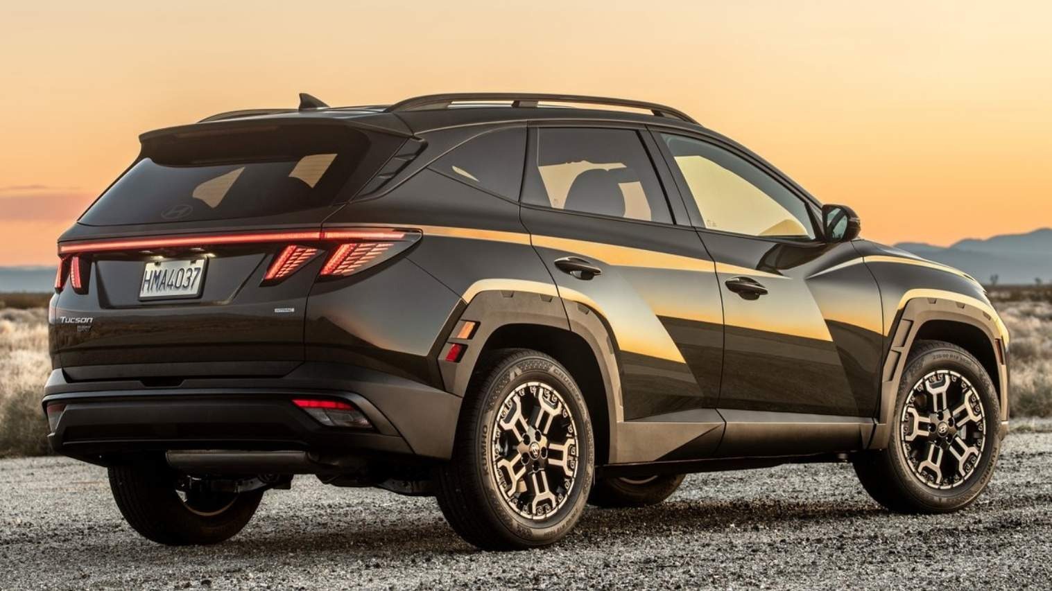 डार्क रंग की Hyundai Tucson Hybrid का रियर क्वार्टर व्यू। इसमें स्पोर्टी कट्स, अनोखी टेल लाइट डिज़ाइन, और मजबूत Hyundai Hybrid SUV प्रोफाइल दिखाई गई है।