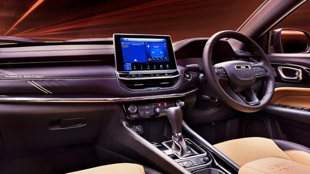 Jeep Compass Track Edition का प्रीमियम इंटीरियर, जिसमें Uconnect 5 टचस्क्रीन इंफोटेनमेंट सिस्टम, डुअल-टोन सीट्स और 'TRACK EDITION' एम्बॉसिंग दिख रही है, जो इसकी Jeep Compass Track Edition Price को सही ठहराते हैं।