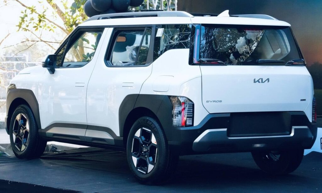Kia Syros EV का पिछला हिस्सा एक इवेंट में प्रदर्शित किया गया, जो Kia Festive Season Offers October 2025 के तहत उपलब्ध है, जिसमें इसकी बॉक्सी डिज़ाइन और वर्टिकल टेललाइट्स दिख रही हैं।