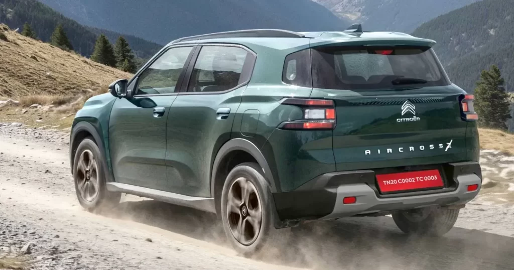Citroen Aircross X का हरे रंग का रियर 3/4 व्यू, जो ऊबड़-खाबड़ इलाके (off-road) में धूल उड़ाते हुए चल रही है। यह 200 मिमी ग्राउंड क्लीयरेंस को दर्शाता है।